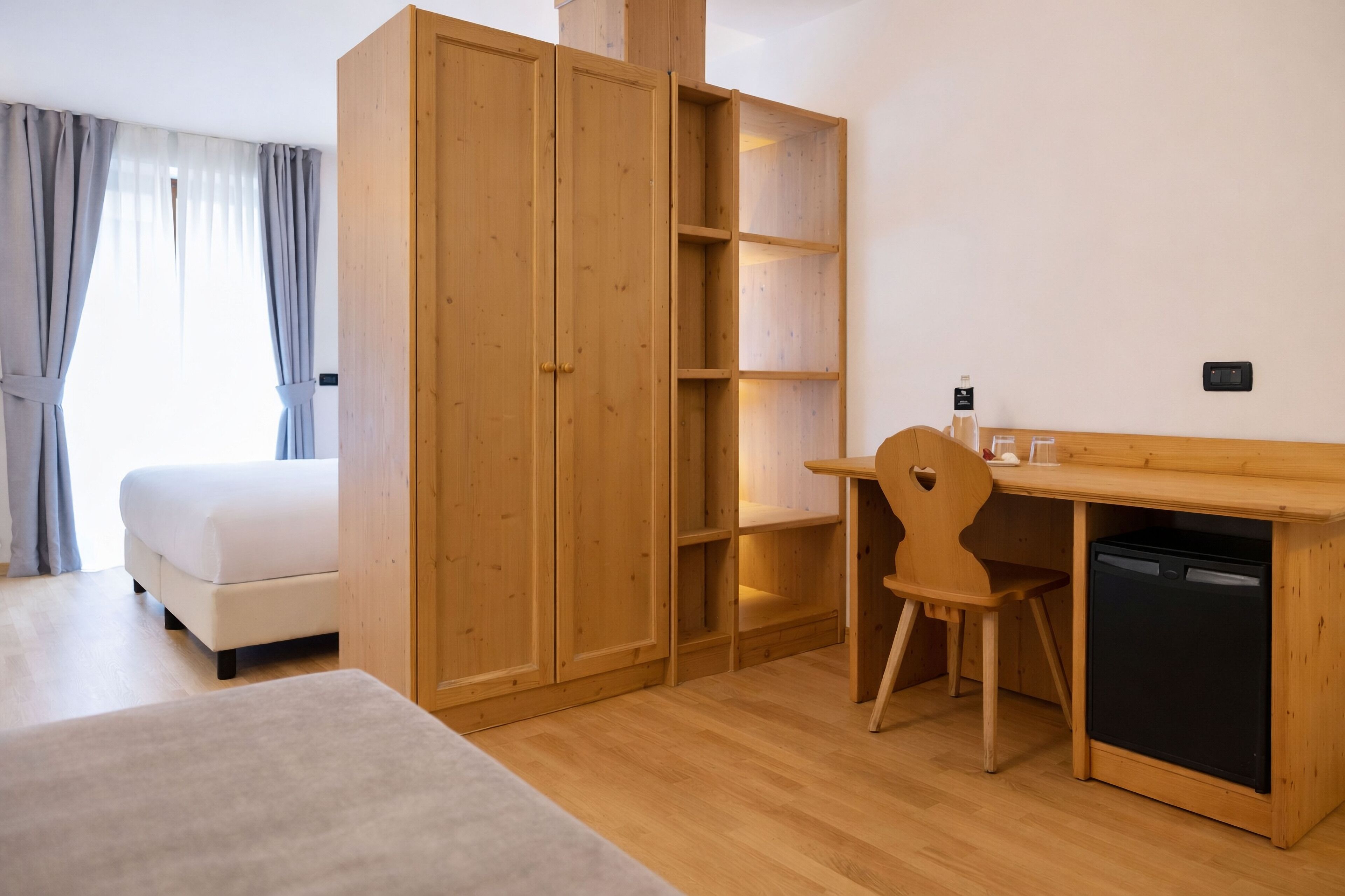 Une chambre comprenant un lit, une armoire en bois, un bureau avec une chaise et un lave-vaisselle encastré.