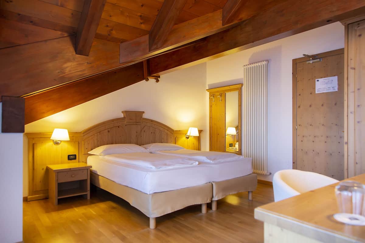 A bedroom with a wooden ceiling, a double bed, bedside lamps, a nightstand, and a wooden door.