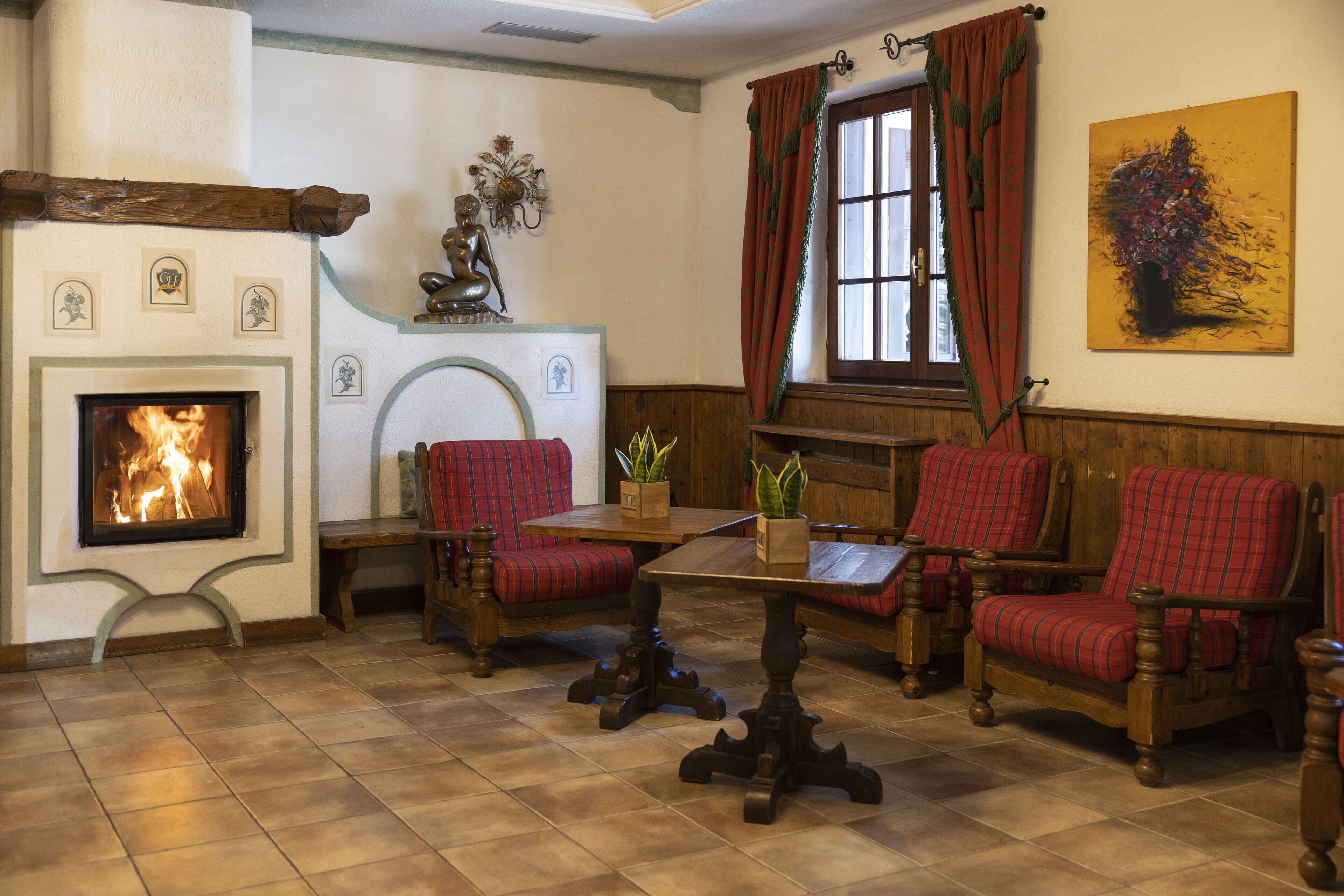A cozy room with a fireplace, red plaid chairs, a wooden table, and a window with curtains.