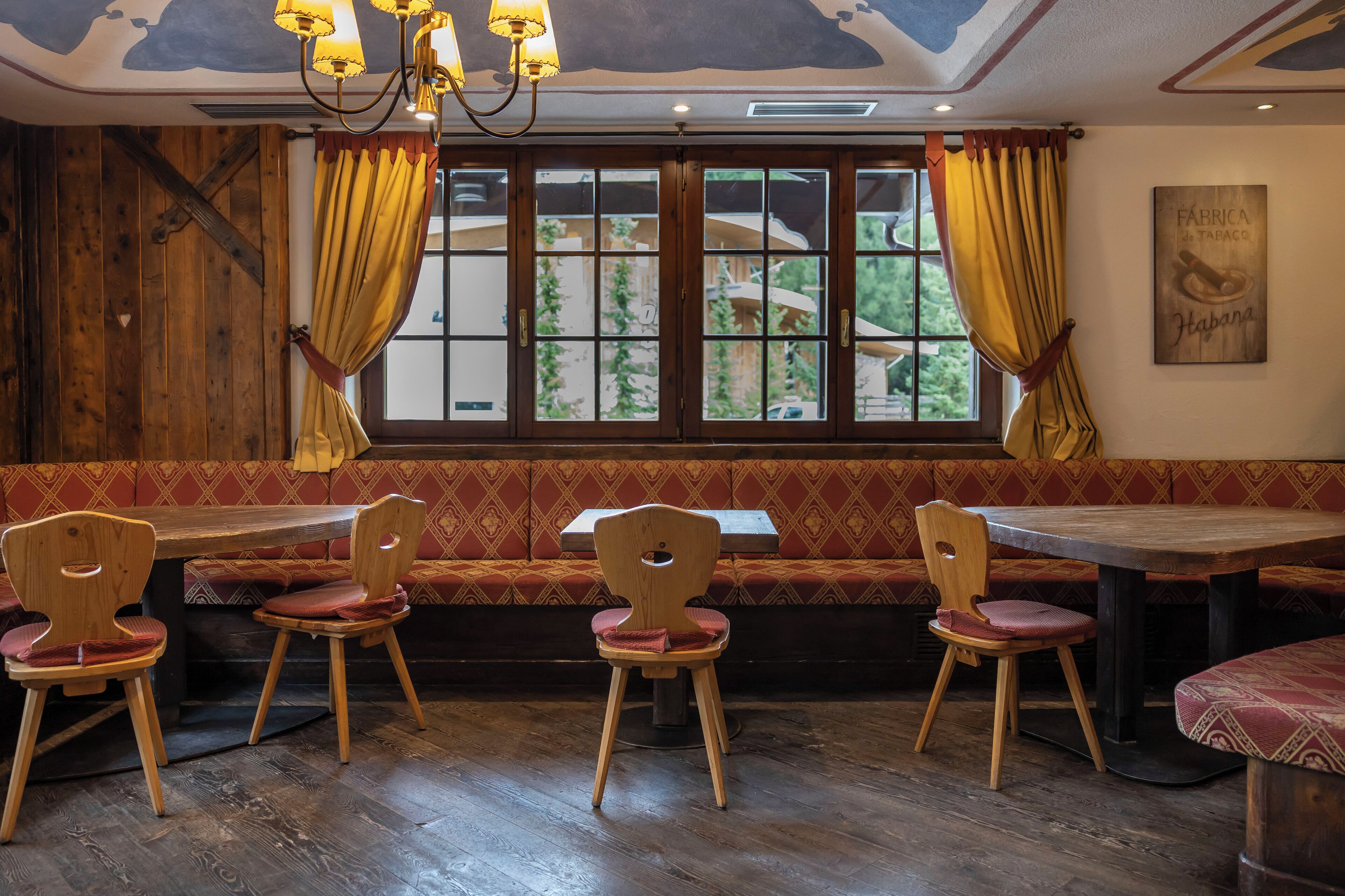 A restaurant with wooden furniture, a large window with curtains, and a ceiling with a skylight.