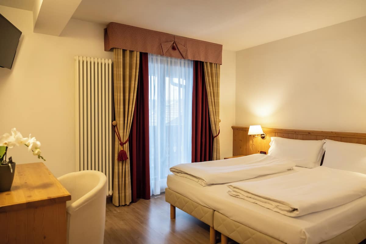 A hotel room with a bed, a desk, a chair, a lamp, and a window with curtains.