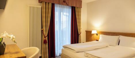 Habitación de hotel con cama, escritorio, silla, lámpara y ventana con cortinas.
