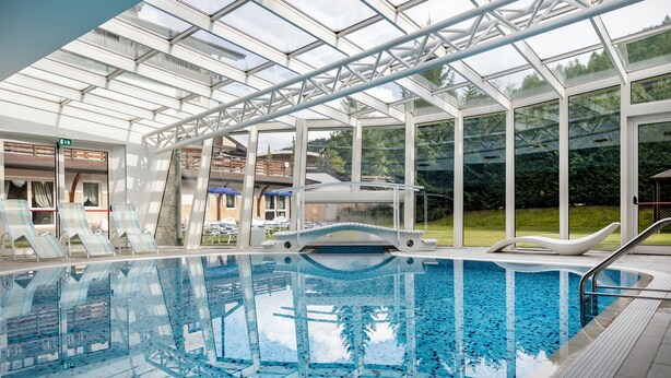Una piscina con techo de cristal, sillas de descanso y un puente sobre el agua.