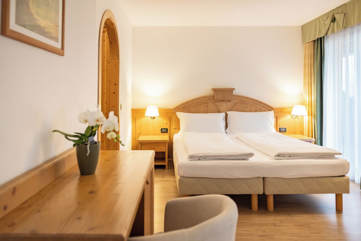 A hotel room with a double bed, wooden headboard, bedside lamps, a wooden desk, and a chair.