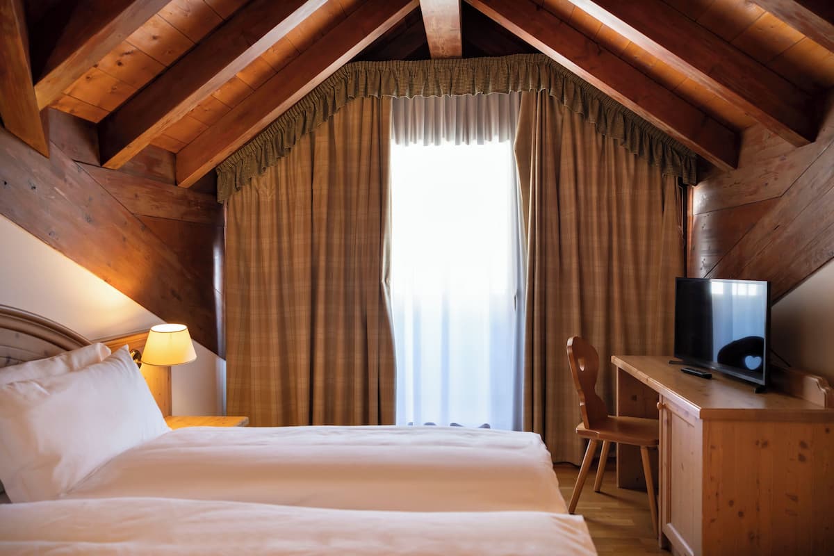 A bedroom with a bed, a desk with a television, a chair, and a window with curtains.