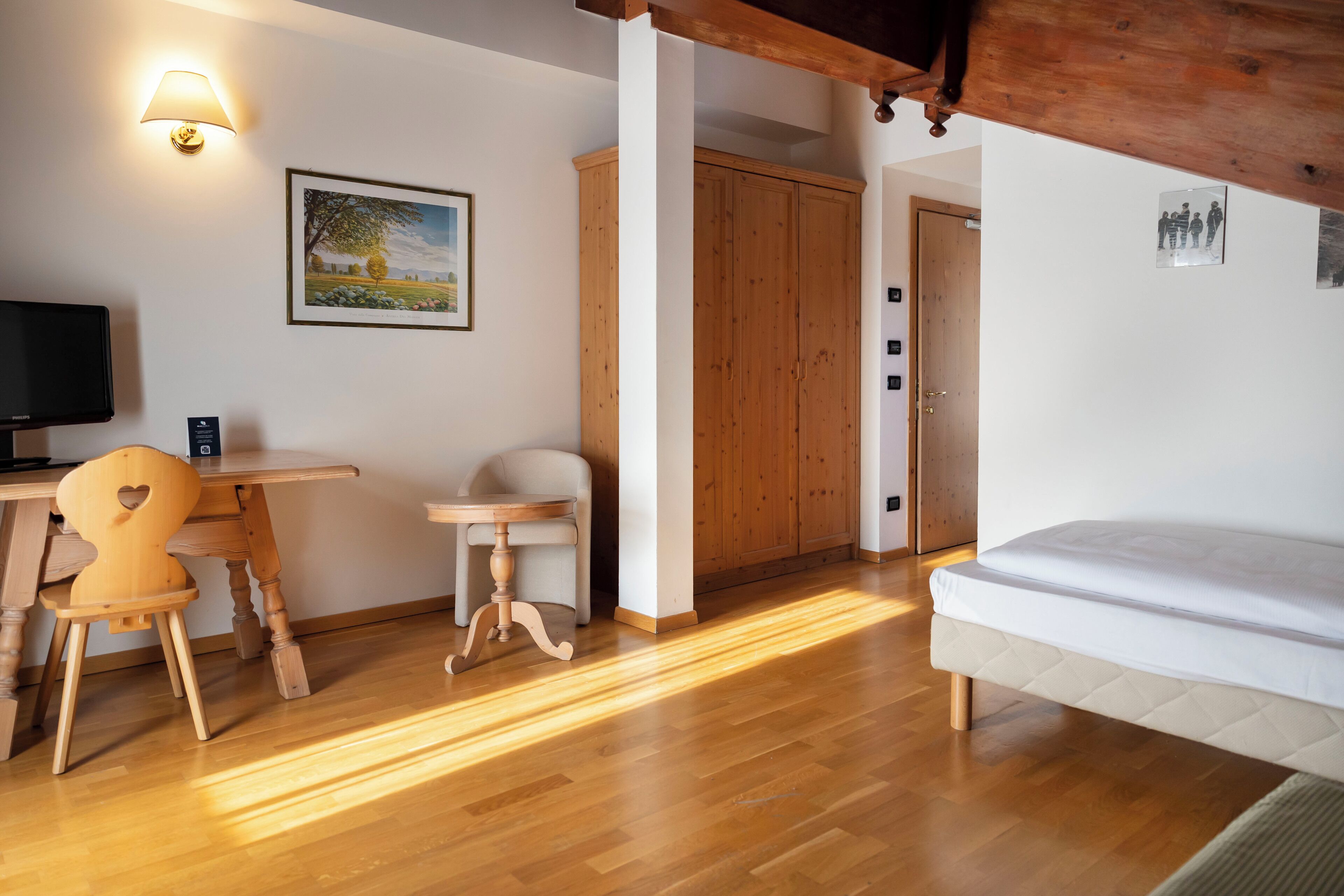 A room with a wooden desk, a chair, a bed, a television, and a wardrobe.