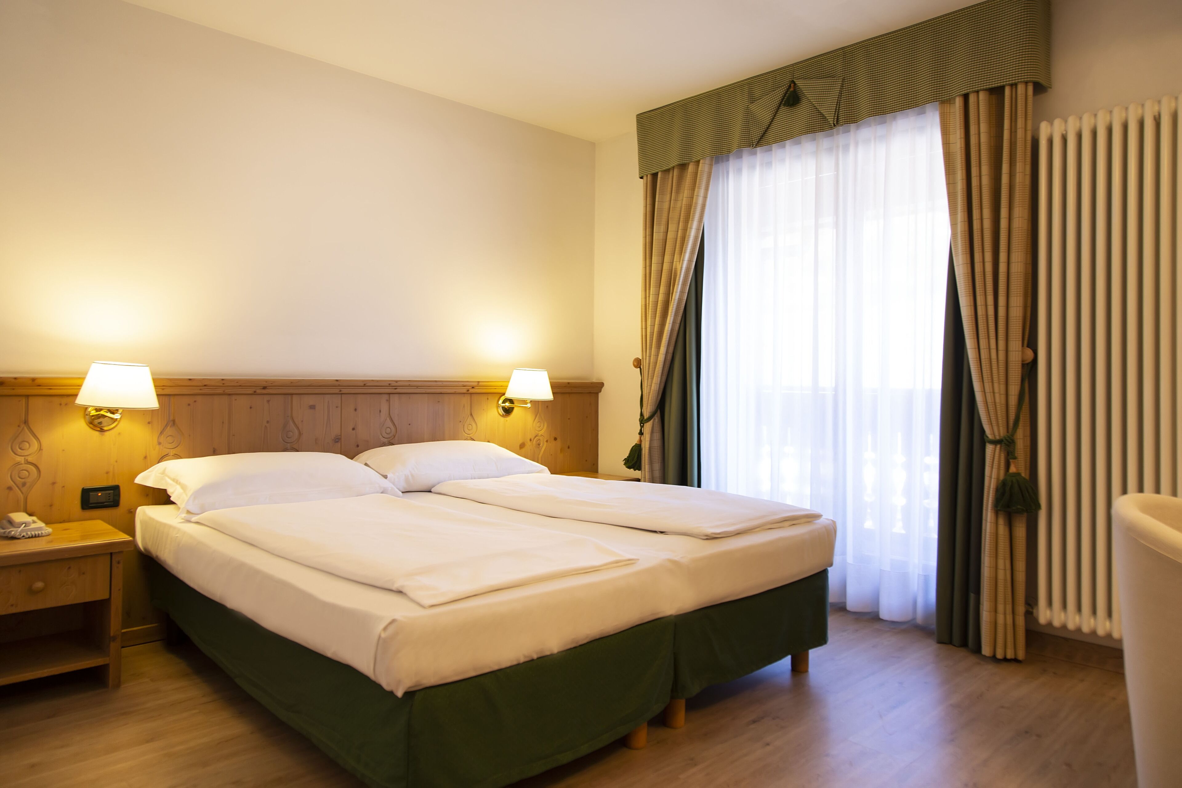 Une chambre d’hôtel avec un lit double, deux lampes de chevet, une table de nuit en bois et une fenêtre avec des rideaux.