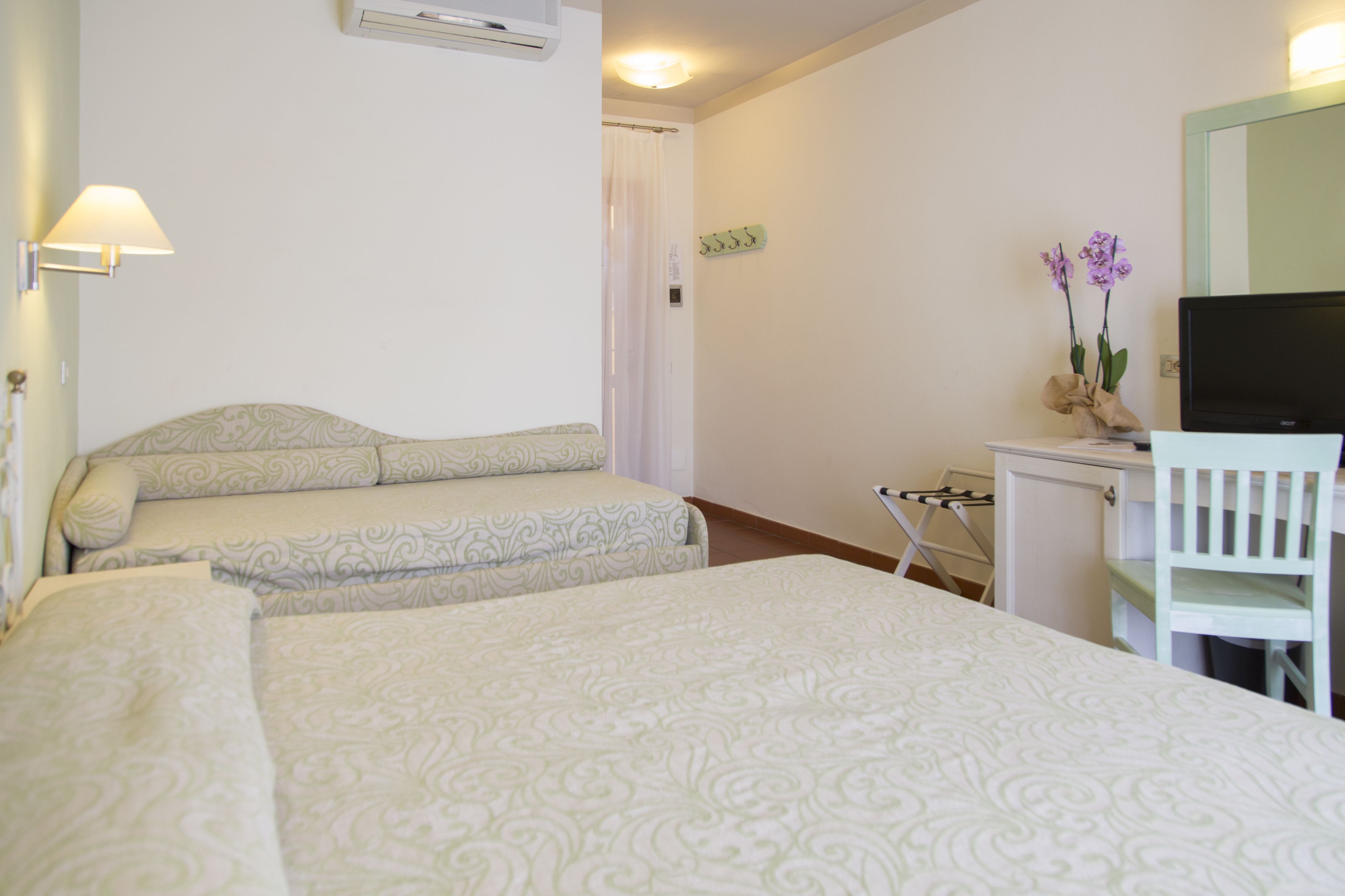 A hotel room with two beds, a desk with a chair, a television, and a small table with a vase of flowers.