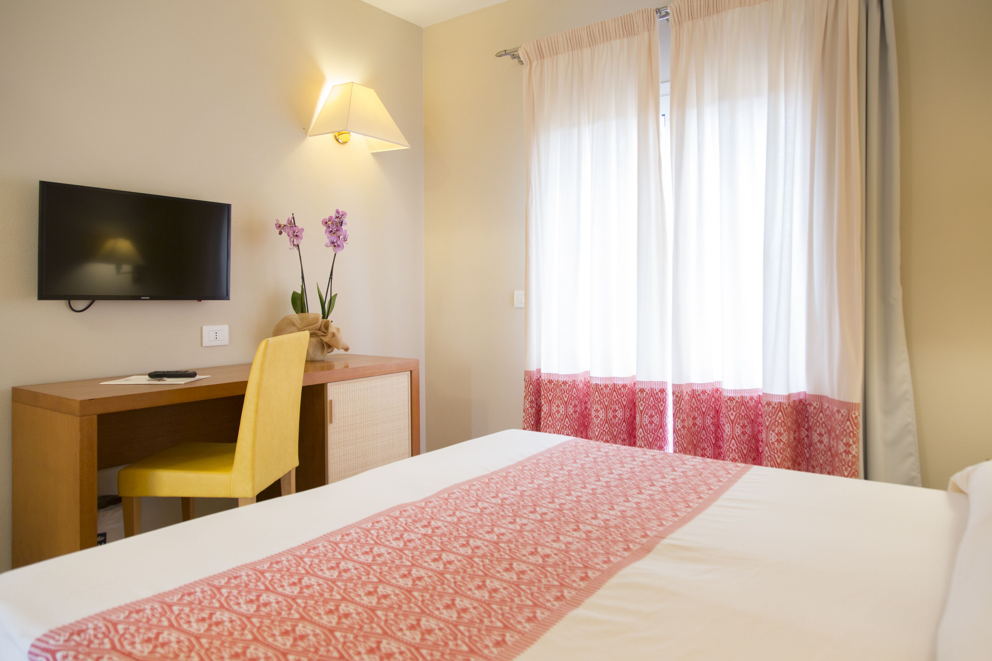 Ein Hotelzimmer mit einem Bett, einem Schreibtisch mit Stuhl, einem Fernseher und einem Fenster mit Vorhängen.