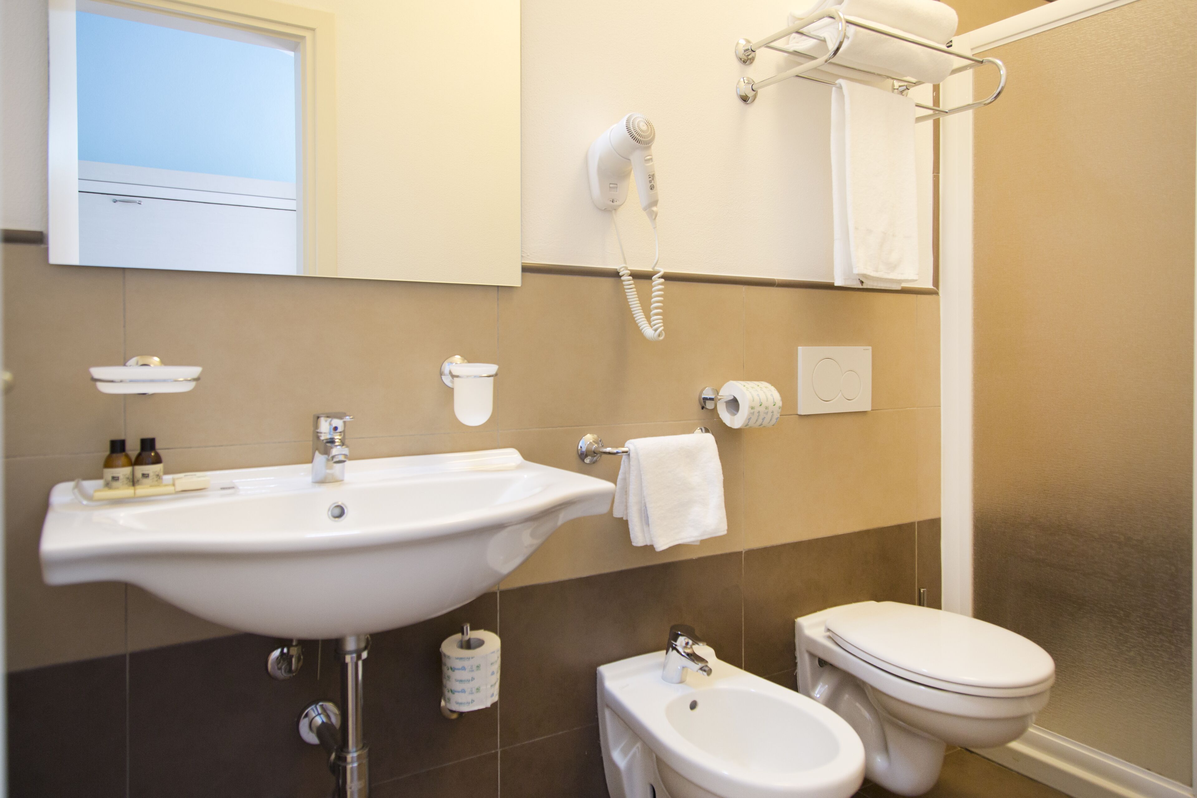 Un bagno con lavandino, wc, bidet e un asciugacapelli fissato alla parete.