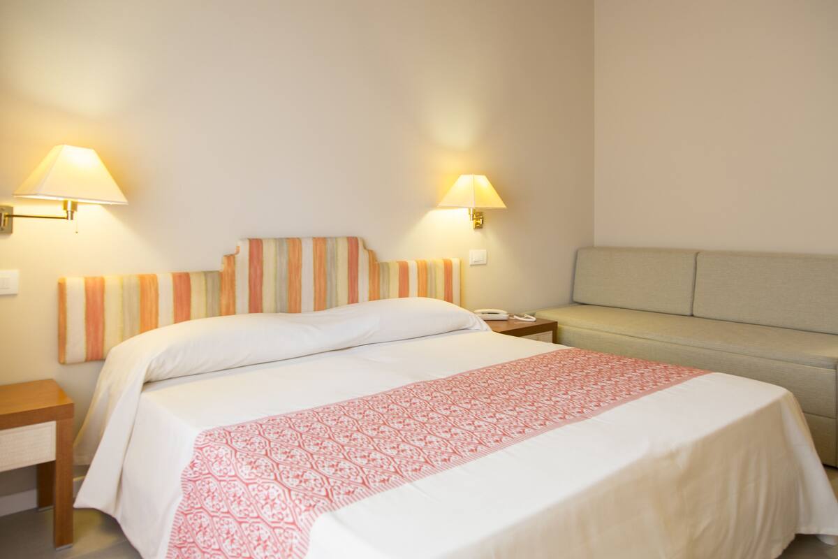A hotel room with a bed, bedside lamps, a nightstand, and a sofa.
