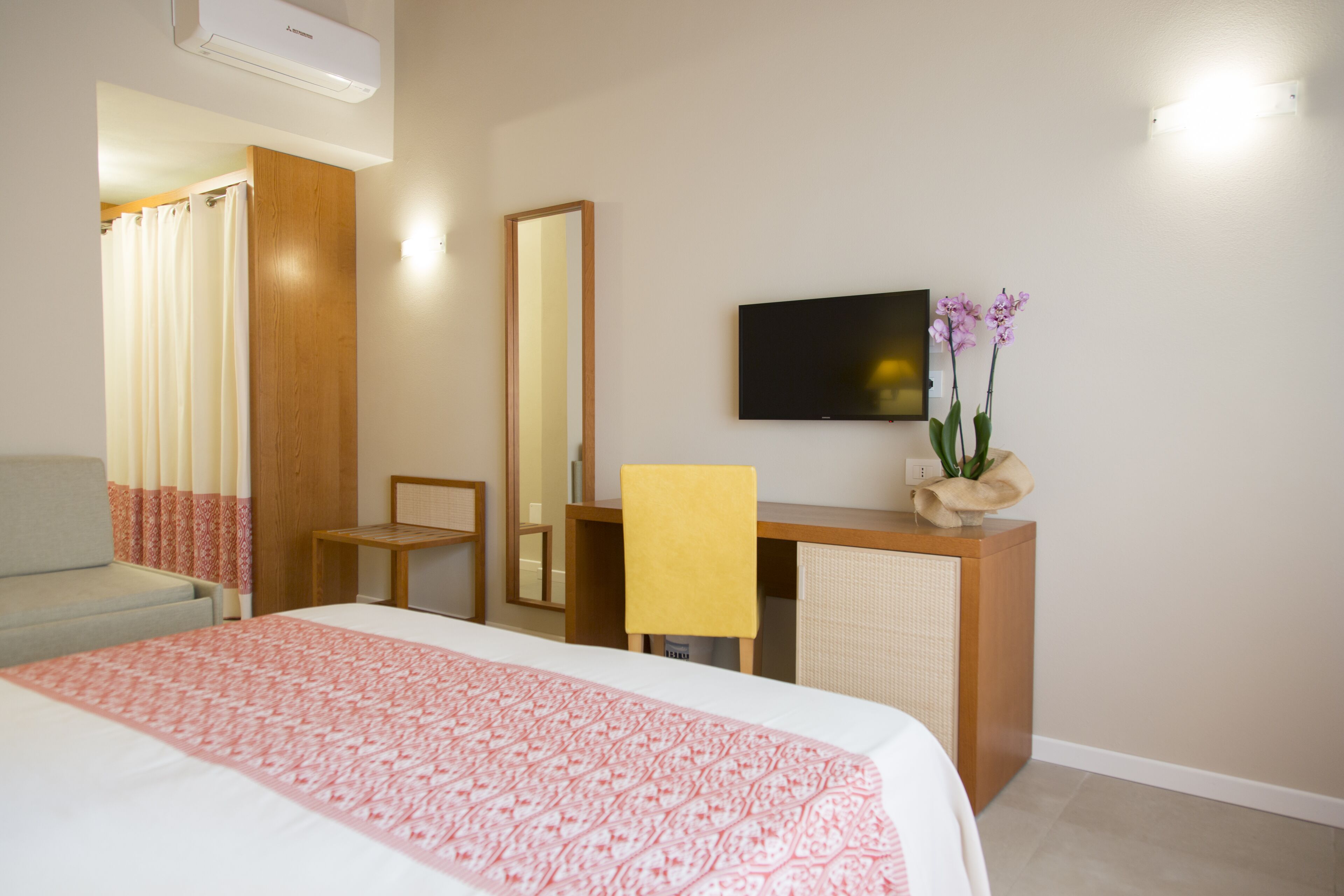Ein Hotelzimmer mit Bett, Schreibtisch, Stuhl, Fernseher und Spiegel.