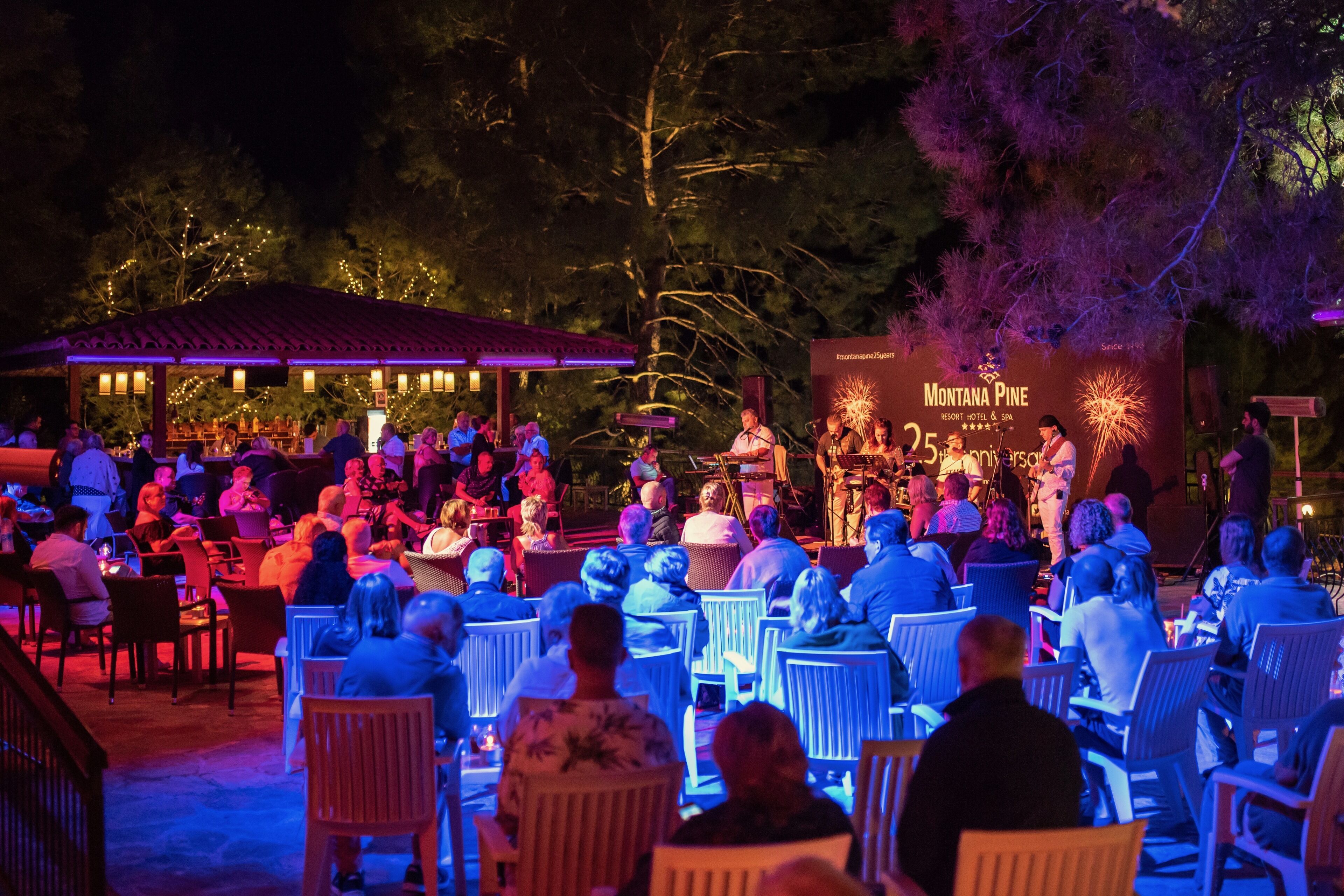 Evento al aire libre con escenario y público sentado en mesas.
