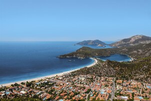 Vista aérea de un pueblo costero con playa, zona residencial y terreno montañoso.