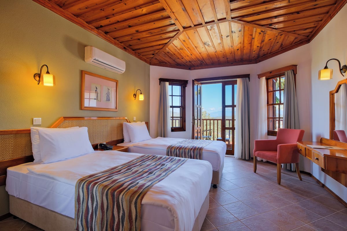 A hotel room with two beds, a desk, a chair, and a balcony with curtains.