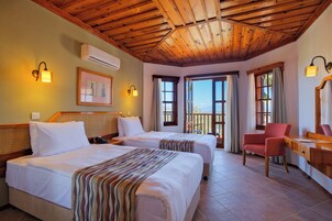 Habitación de hotel con dos camas, un escritorio, una silla y un balcón con cortinas.