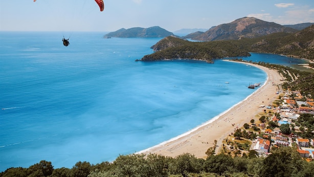 Une zone côtière comprenant une plage, une petite ville et des montagnes en arrière-plan.