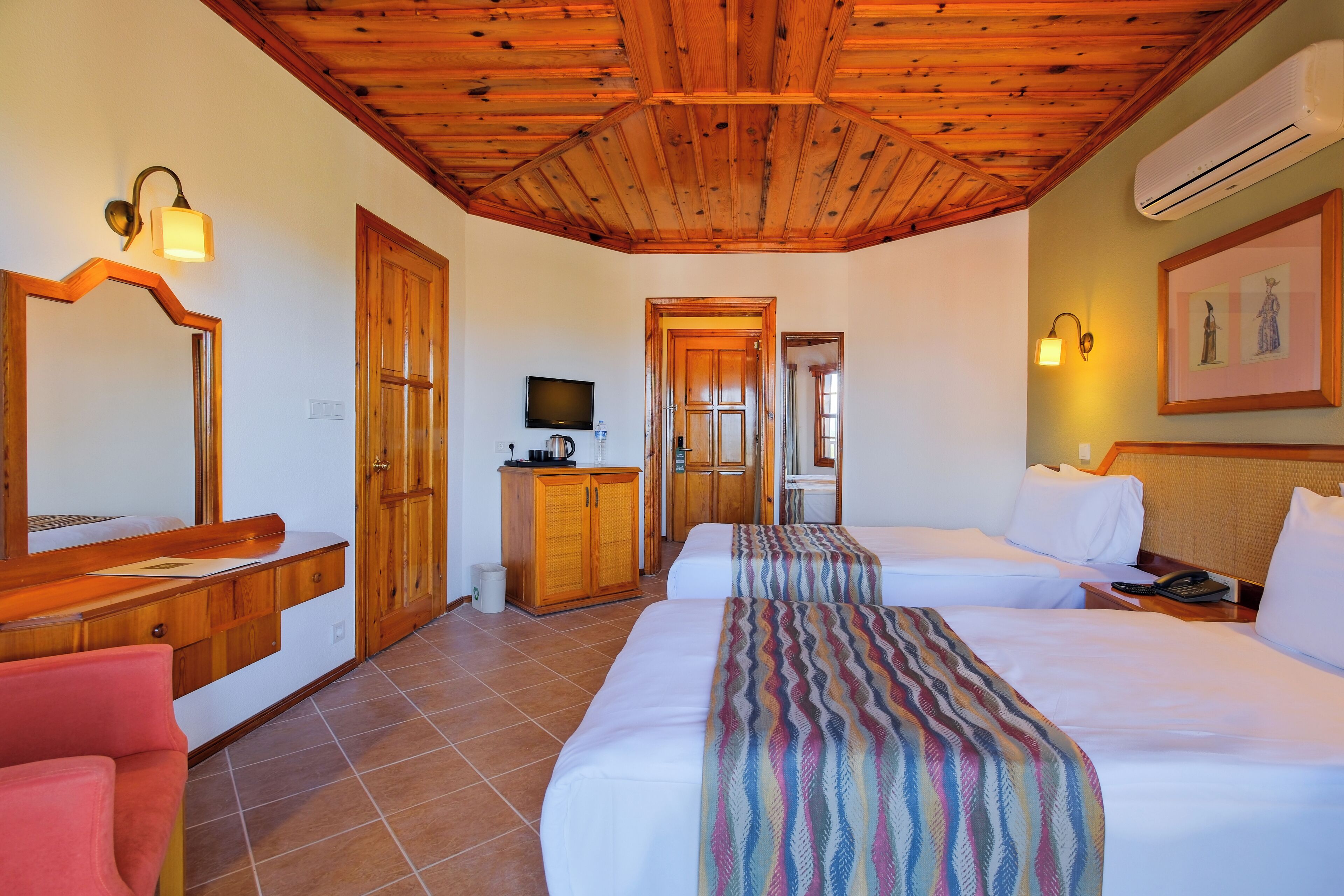 A hotel room with two beds, a wooden ceiling, a TV, a minibar, and a bathroom door.