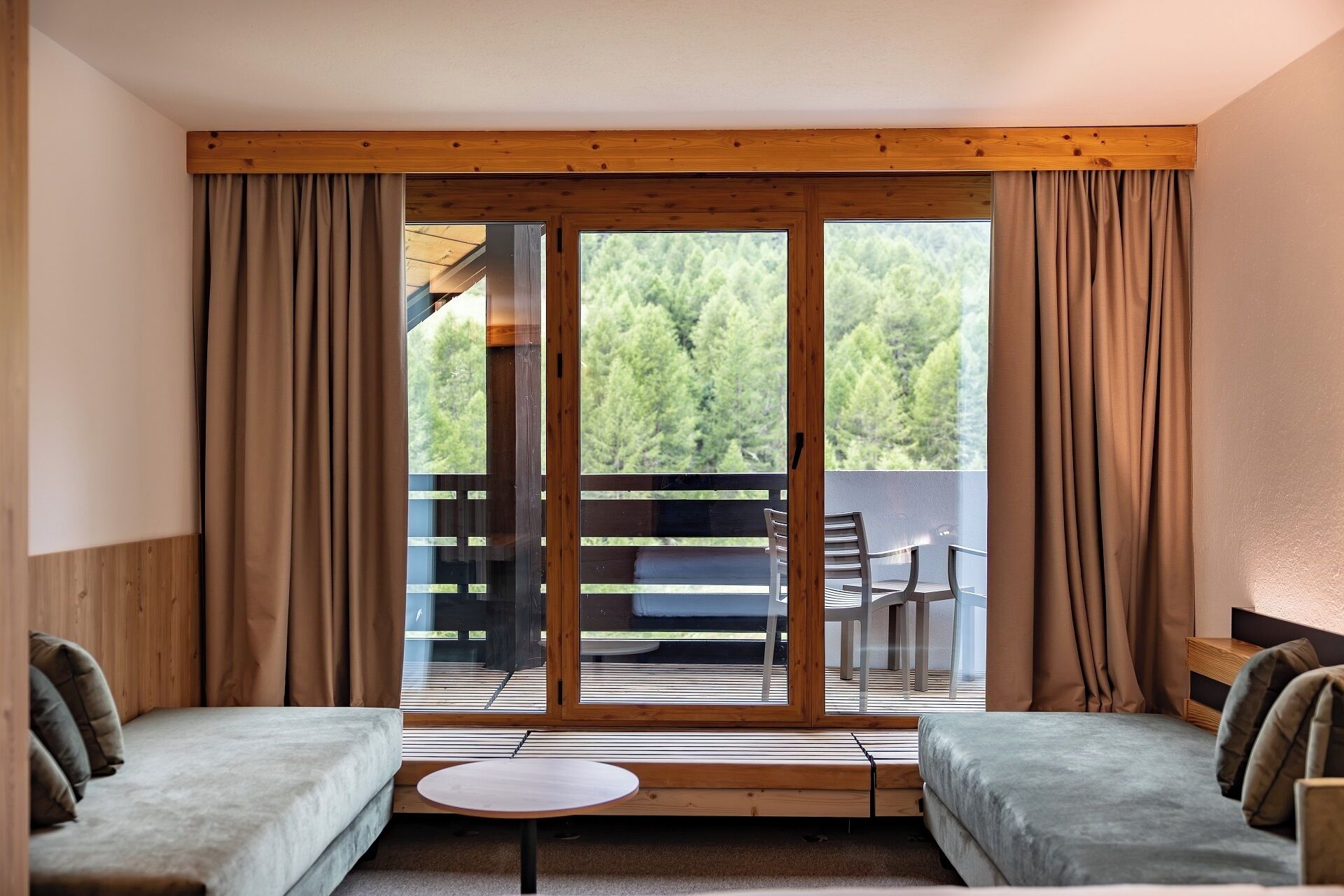 A room with a wooden ceiling, a sliding glass door leading to an outdoor area with a table and chairs, and two beds.