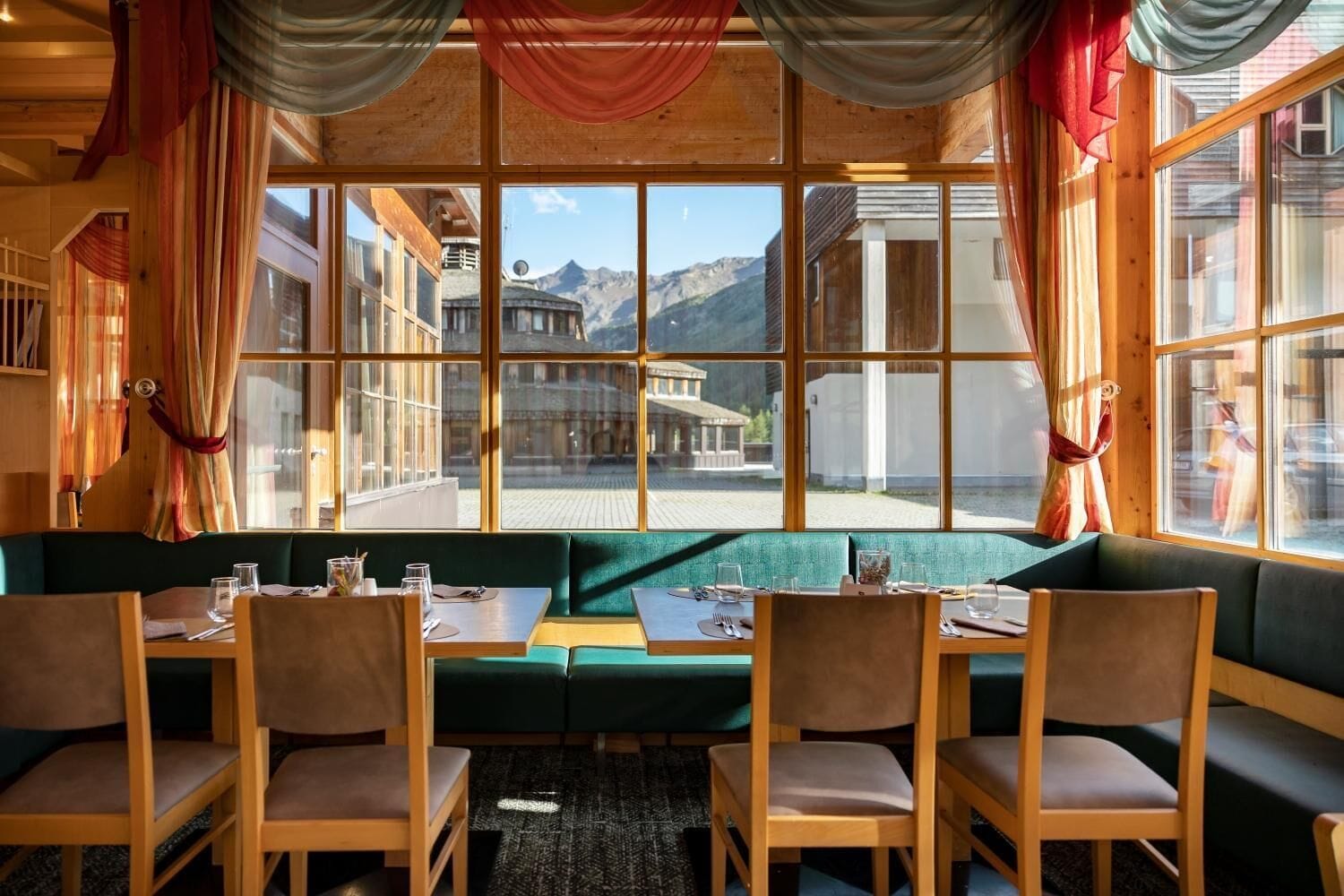 Un restaurant doté d’un coin salon avec des banquettes vertes, de tables et des chaises en bois, et de grandes fenêtres offrant une vue sur les montagnes.