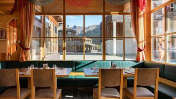 Un restaurant doté d’un coin salon avec des banquettes vertes, de tables et des chaises en bois, et de grandes fenêtres offrant une vue sur les montagnes.