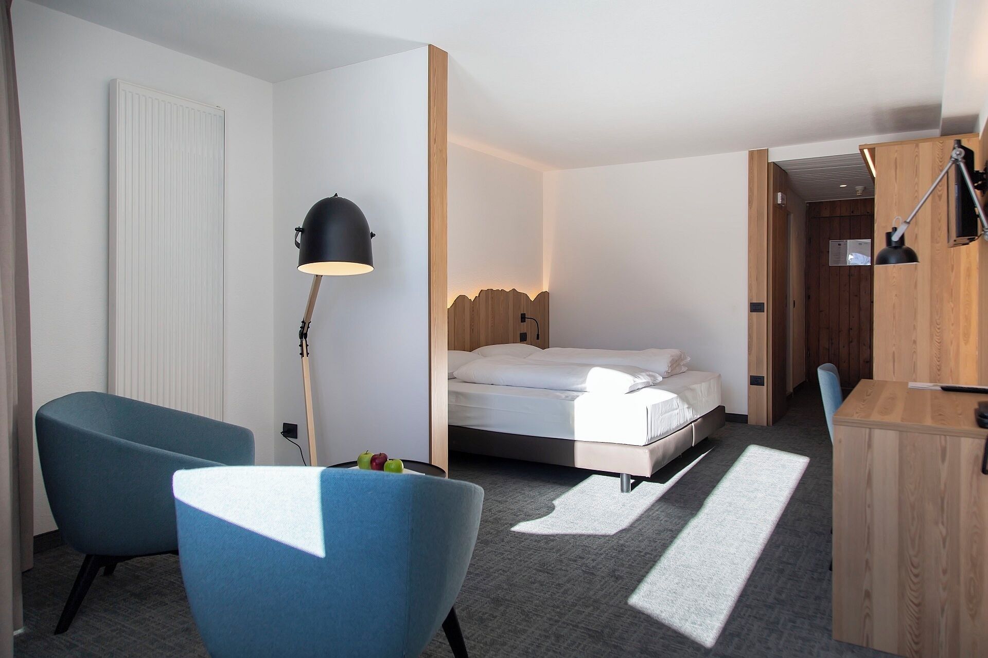A hotel room with a bed, a desk, a chair, a floor lamp, and a wardrobe.