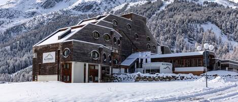 A modern building with a wooden facade and circular windows, set against a snowy mountain backdrop.