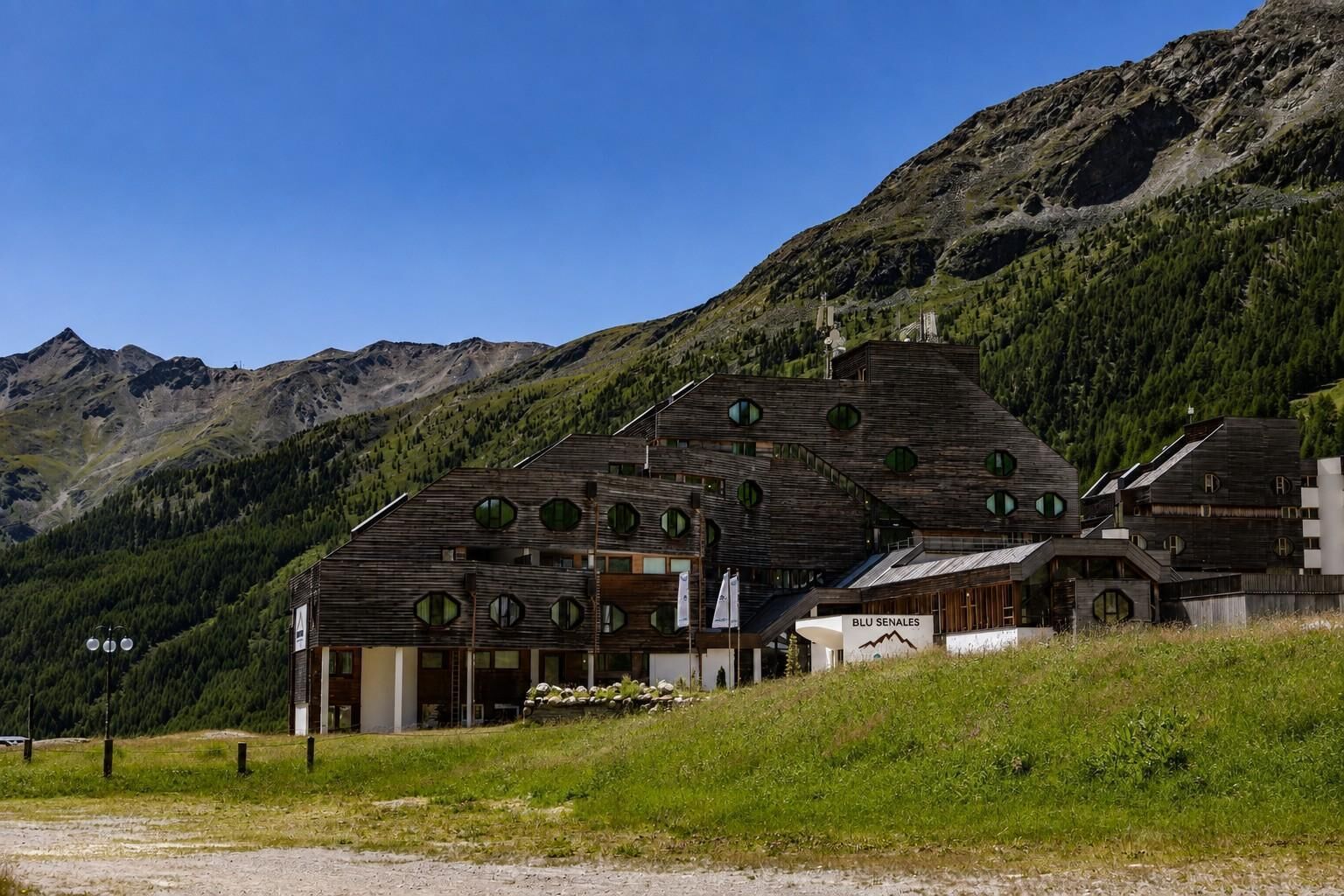 A wooden chalet with multiple windows, set against a mountainous backdrop.