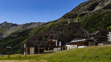 A wooden chalet with multiple windows, set against a mountainous backdrop.