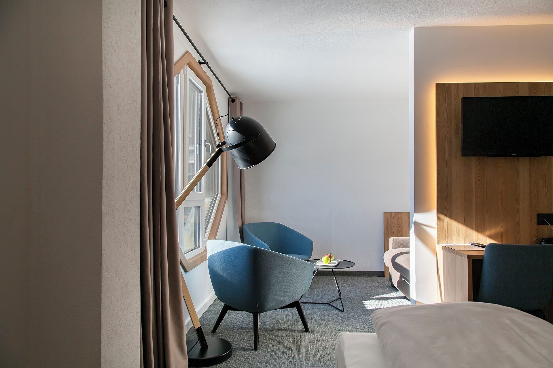 Une chambre d’hôtel avec un lit, deux chaises, un bureau, une télévision et une fenêtre avec des rideaux.