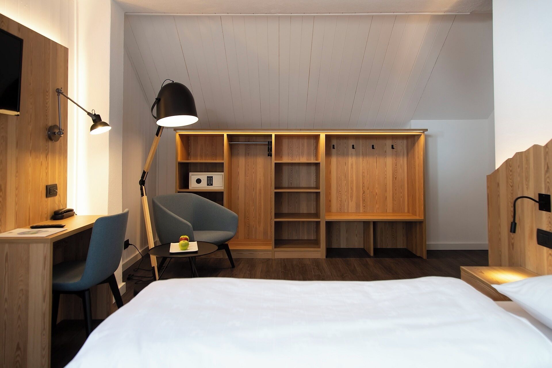 A modern bedroom with a bed, a desk, a chair, a wardrobe, and a desk lamp.