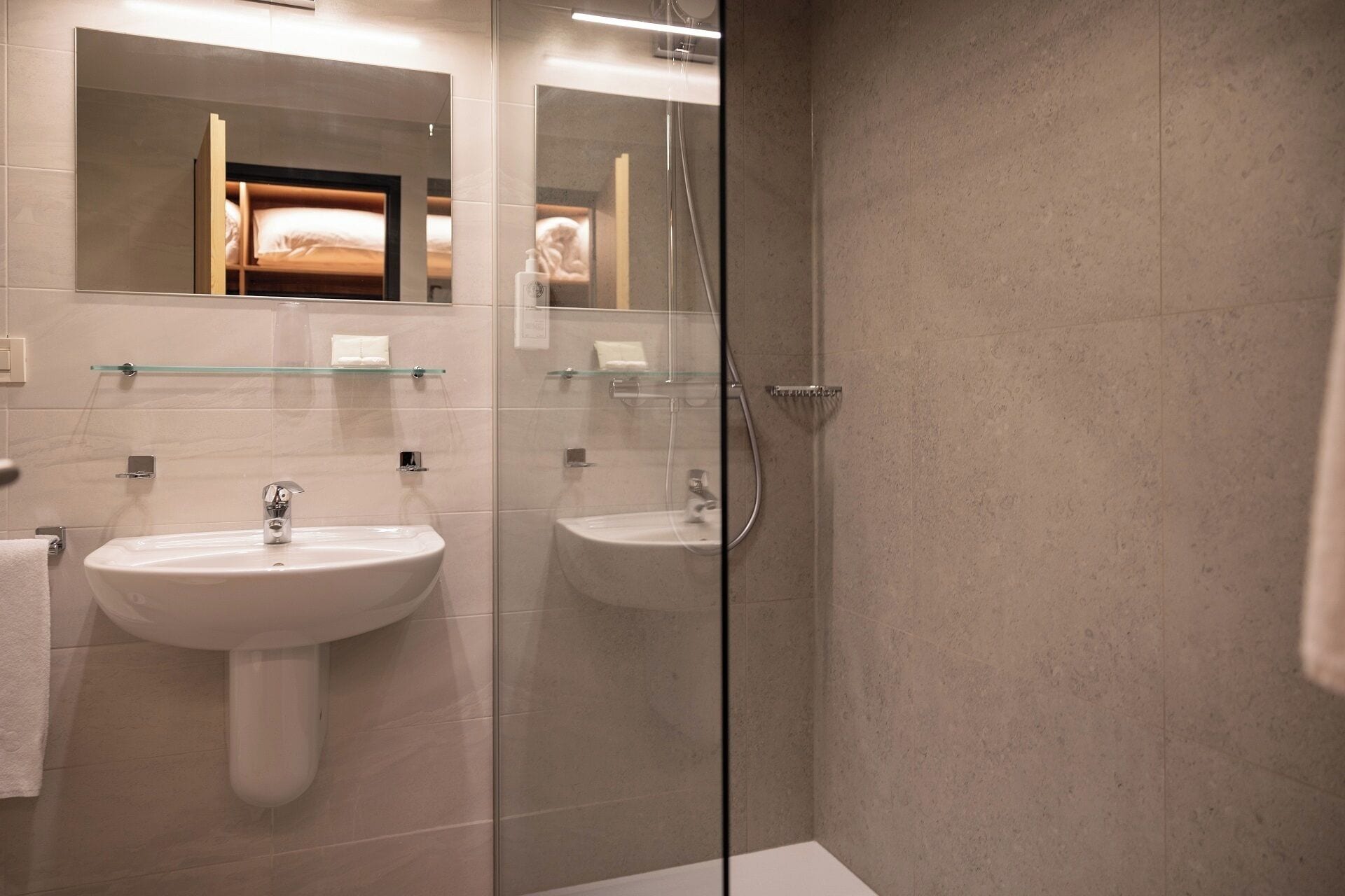 A modern bathroom with two sinks, a glass shower enclosure, and a large mirror.