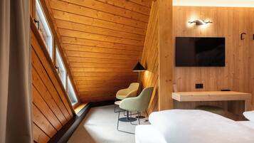 Ein Hotelzimmer mit schräg versiegelter Decke, Holzvertäfelung, einem flachbildfernseher, der über einer Holzkonsole angebracht ist, zwei Sessel und ein Bett.