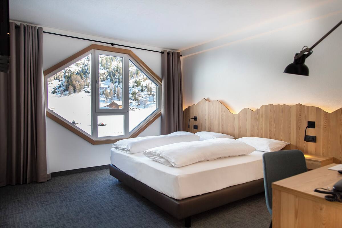 Une chambre d’hôtel avec une grande fenêtre, un lit, un bureau et une lampe.