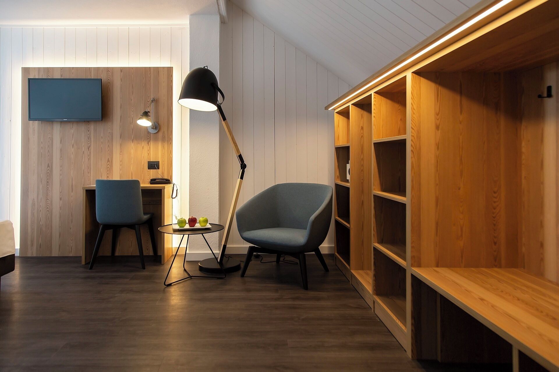Ein modernes Wohnzimmer mit Flachbildfernseher, zwei Sessel, einem Tisch mit Äpfeln, einer Stehlampe und integrierten Holzbögen.