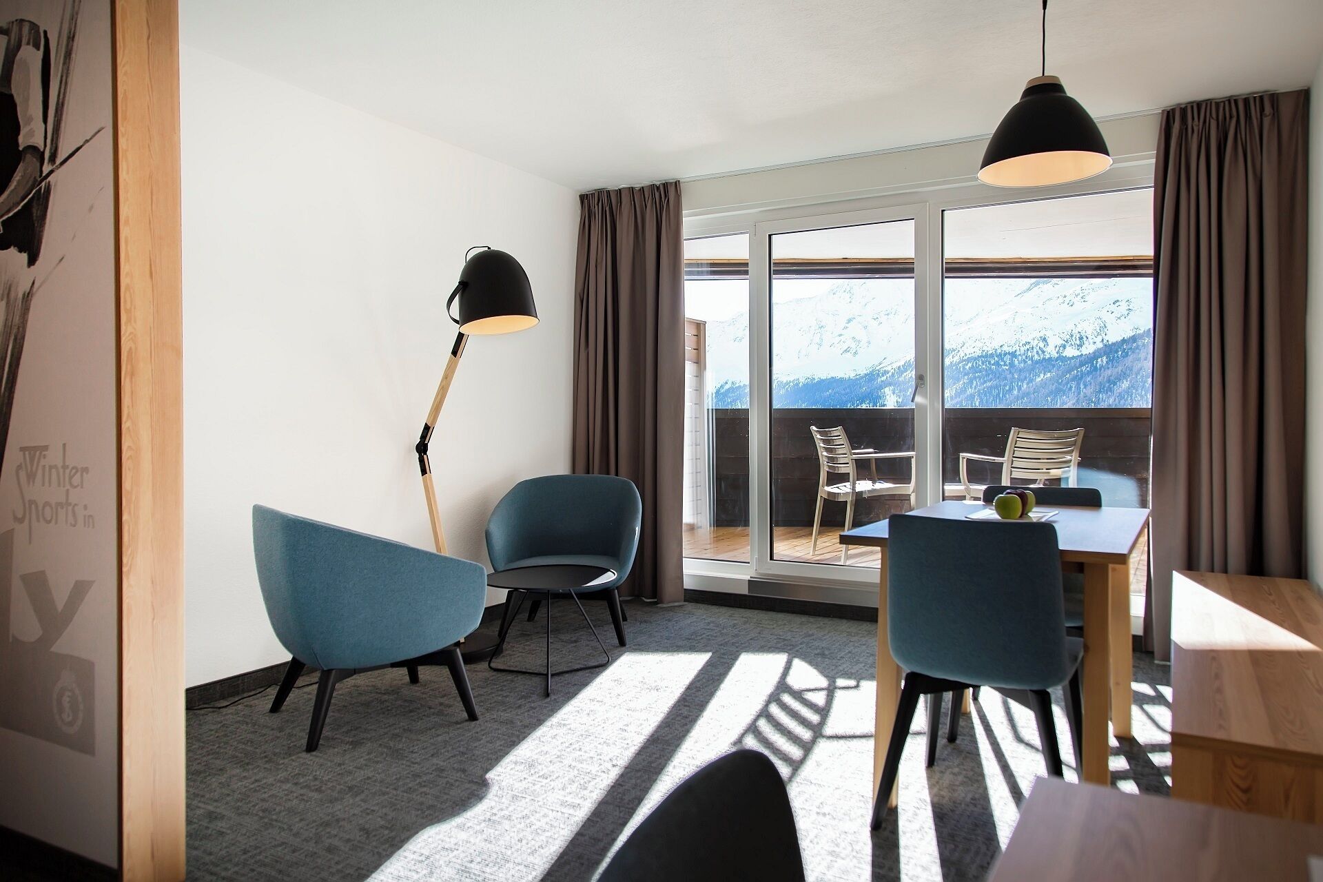 A hotel room with a balcony, two chairs, a table, and a floor lamp.