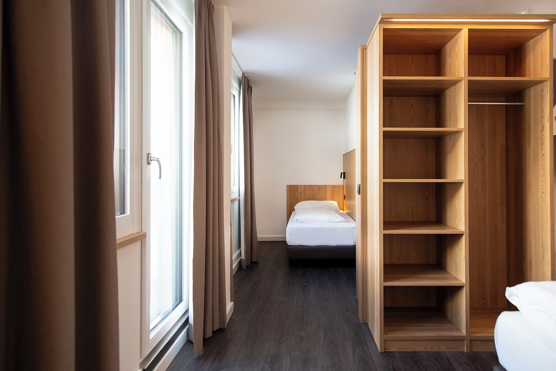 Een hotelkamer met een bed, een houten garderobe en een raam met gordijnen.