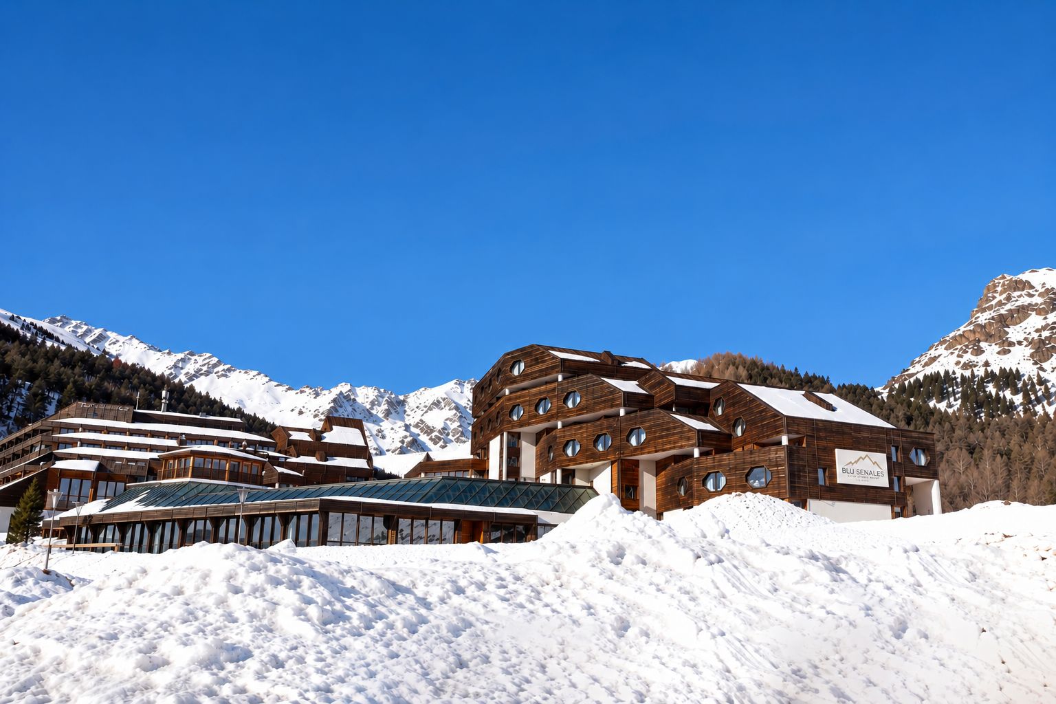 Ein modernes, mehrgeschossiges Gebäude mit großen Fenstern, umgeben von schneebedeckten Bergen.