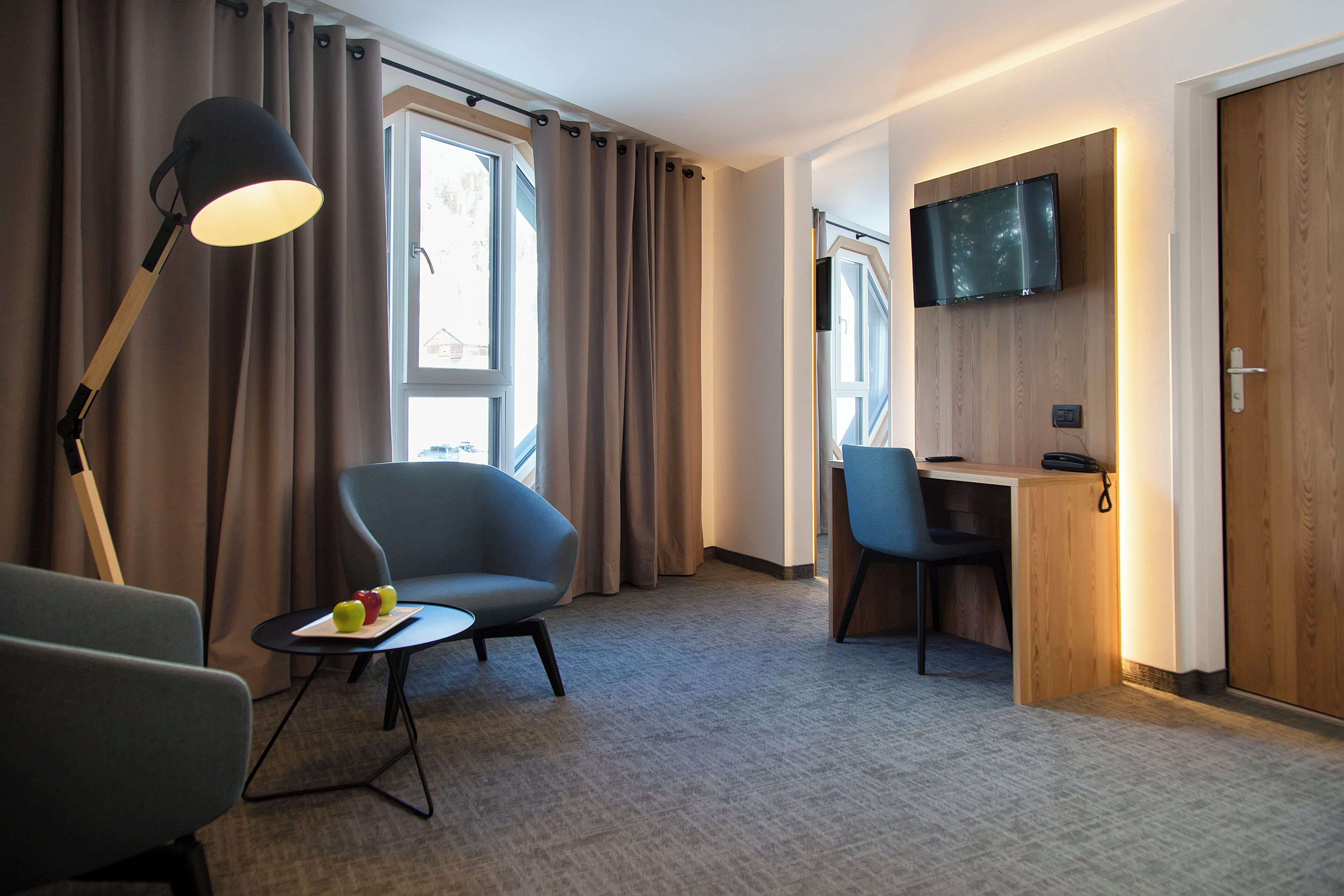 A hotel room with a desk, chair, lamp, and TV.