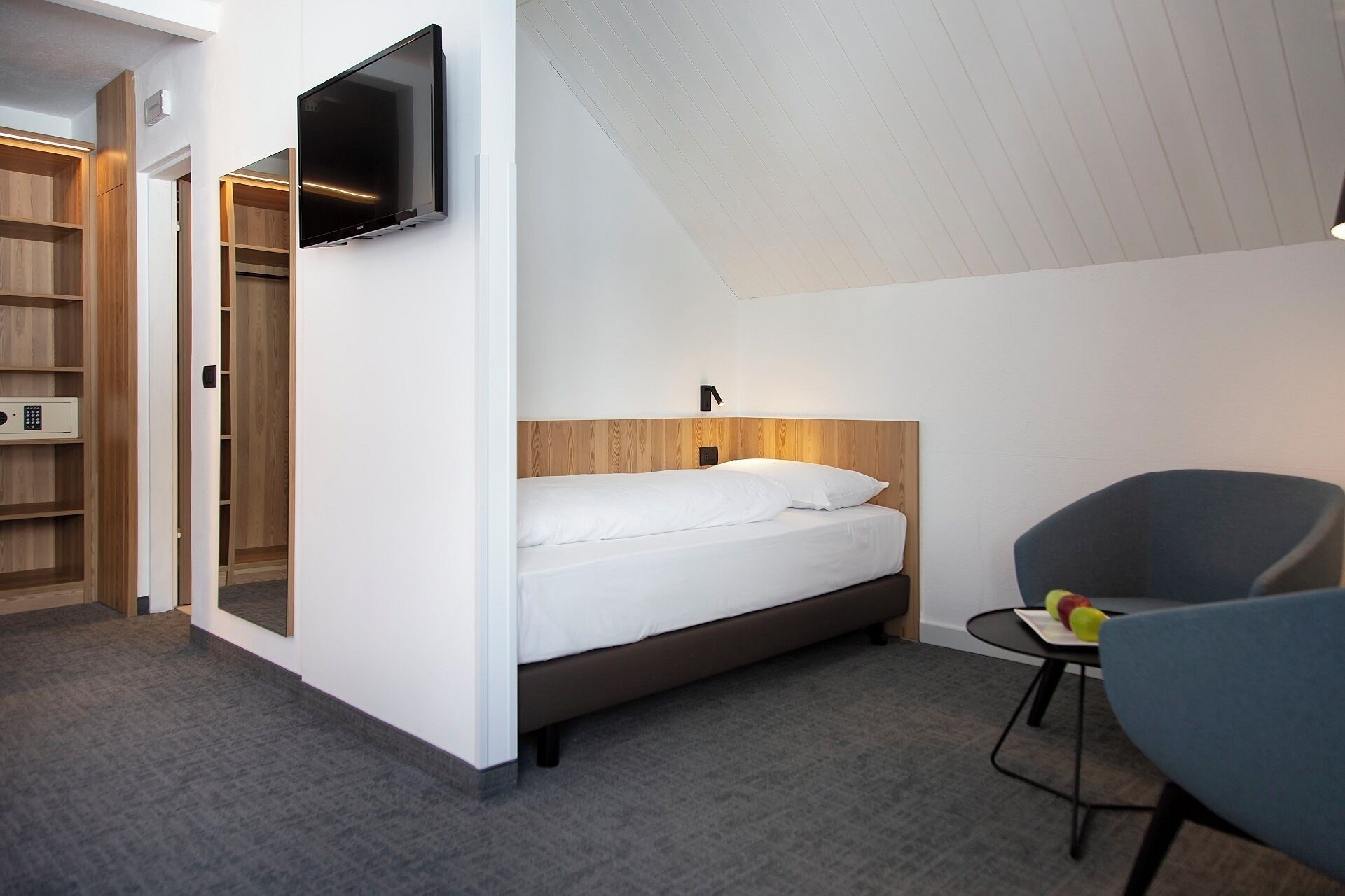Une chambre à coucher comprenant un lit, un téléviseur fixé au mur, un bureau avec une chaise et une armoire.