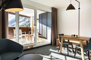 Ein modernes Zimmer mit einem Holztisch, Stühlen und Blick auf einen verschneiten Berg durch eine Glastür.