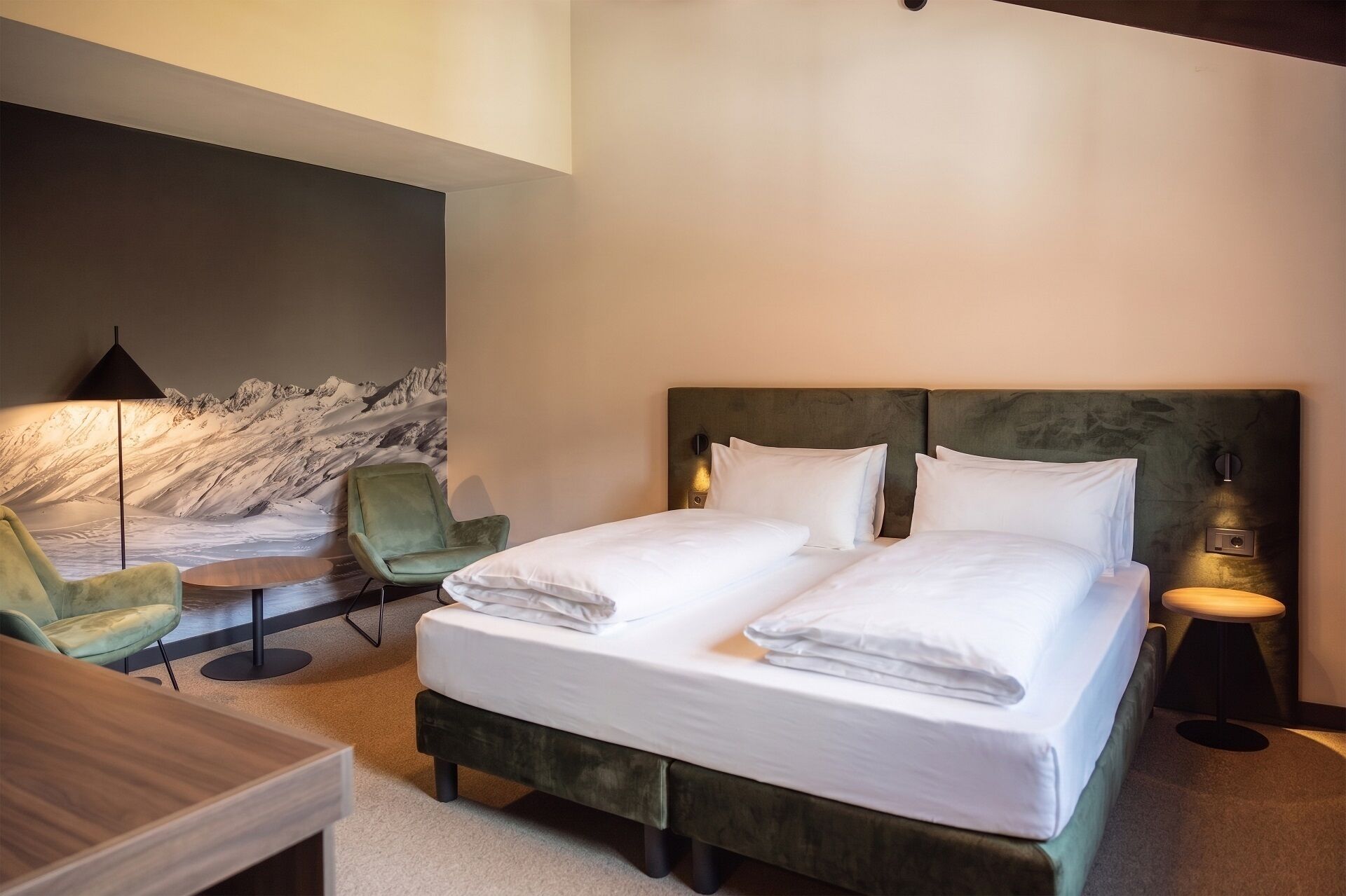 Habitación de hotel con cama, escritorio, silla y lámpara de pared.
