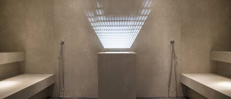 A modern shower area with a central light fixture, benches, and tiled flooring.