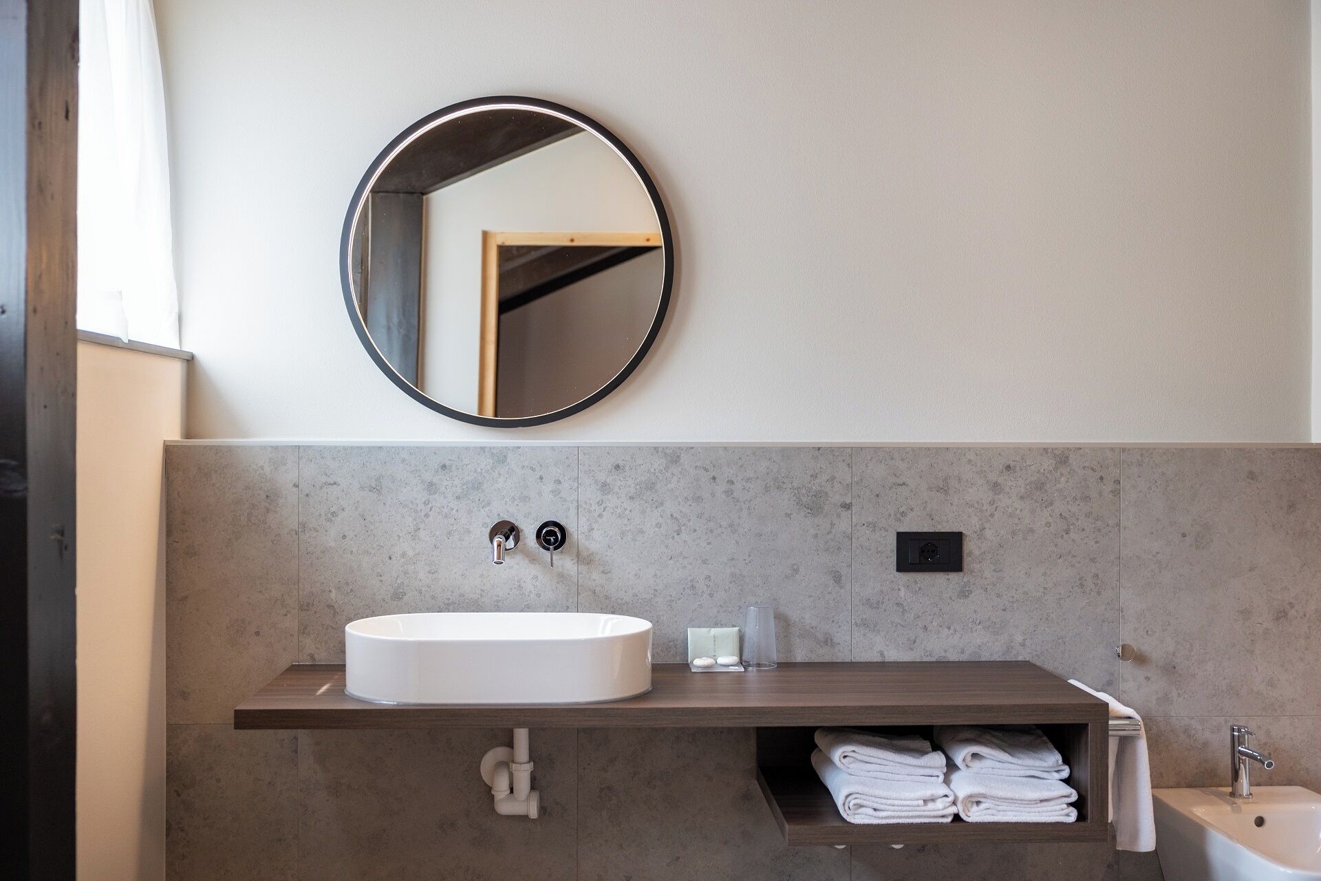 A modern bathroom with a round mirror, a white sink, and a towel rack.