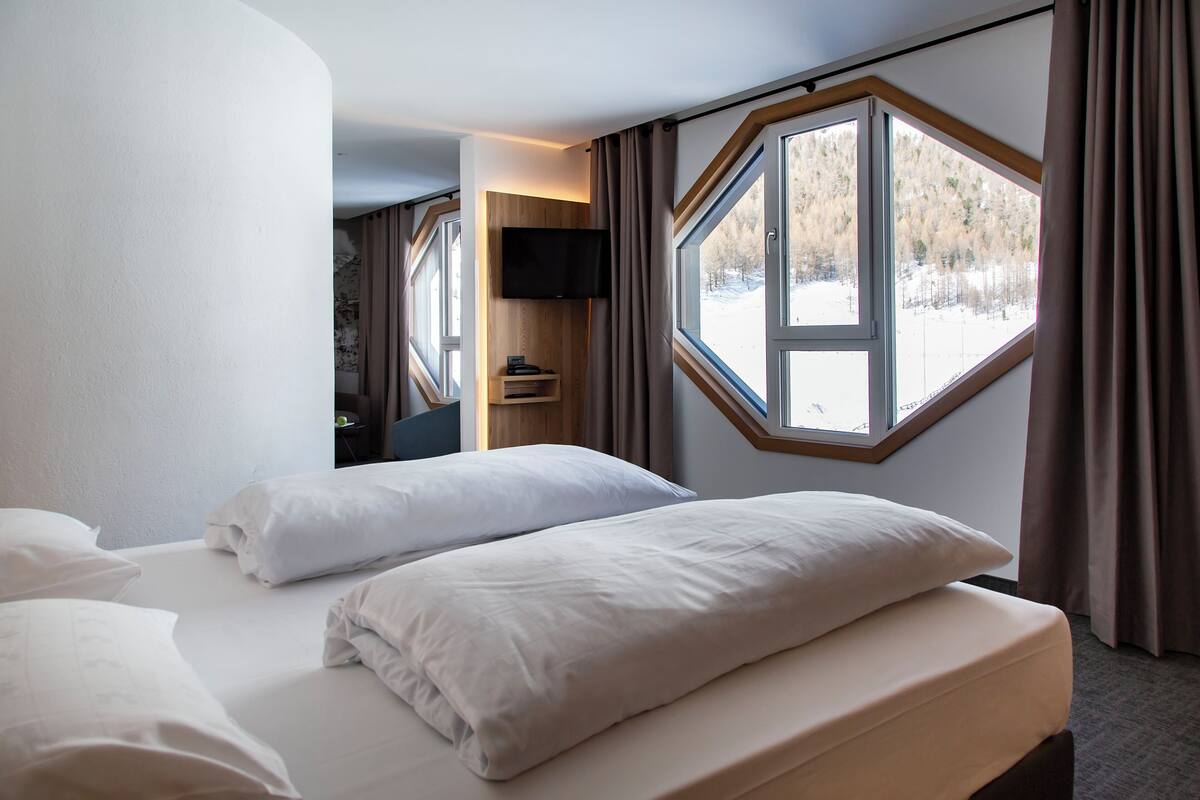 Une chambre d’hôtel dotée d’une grande fenêtre, d’un téléviseur à écran plat et d’un lit avec du linge de lit blanc.