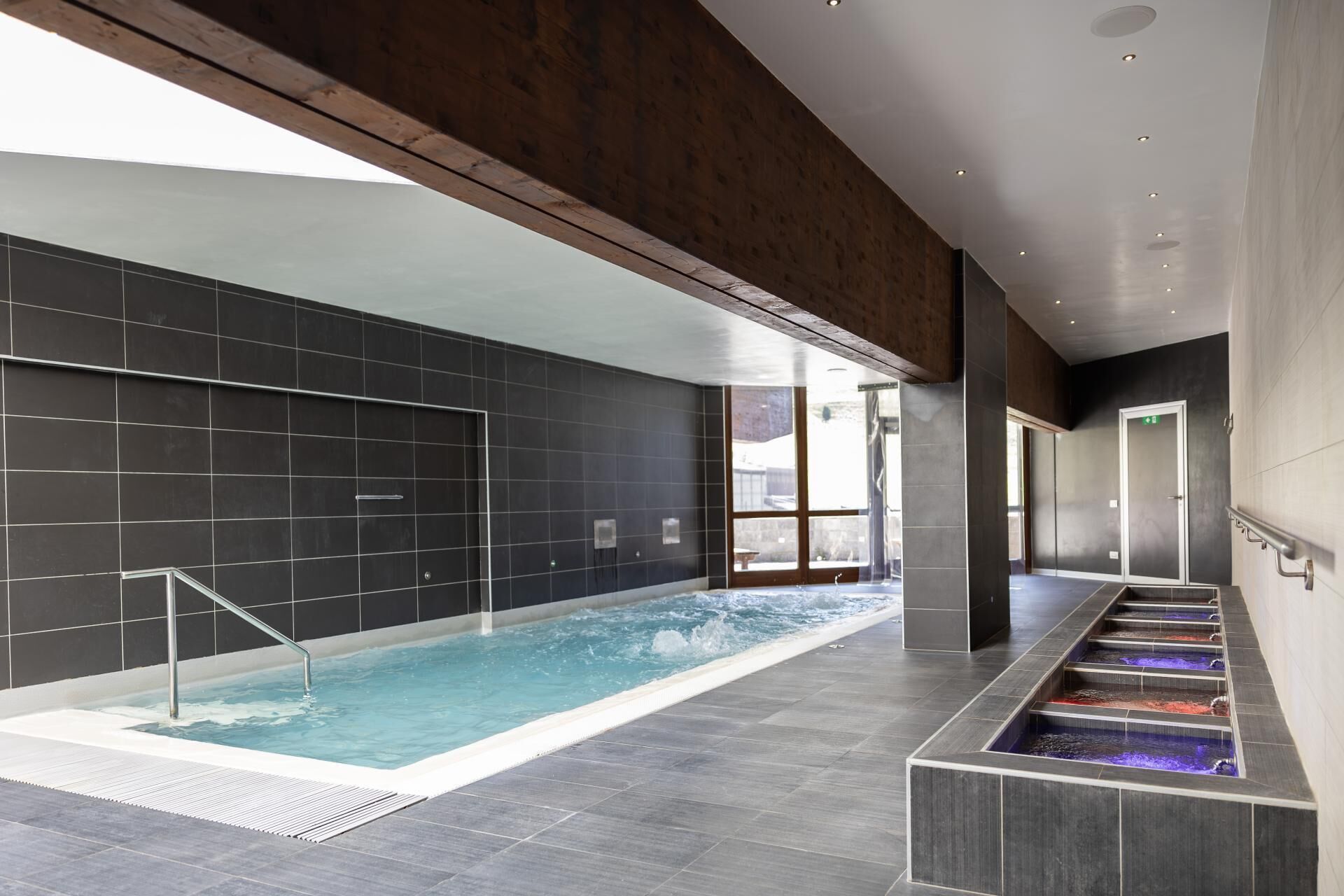 A modern indoor swimming pool with a clear view of the surrounding area, including a staircase and a door.