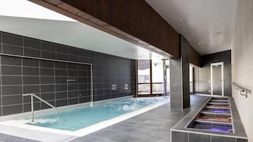A modern indoor swimming pool with a clear view of the surrounding area, including a staircase and a door.