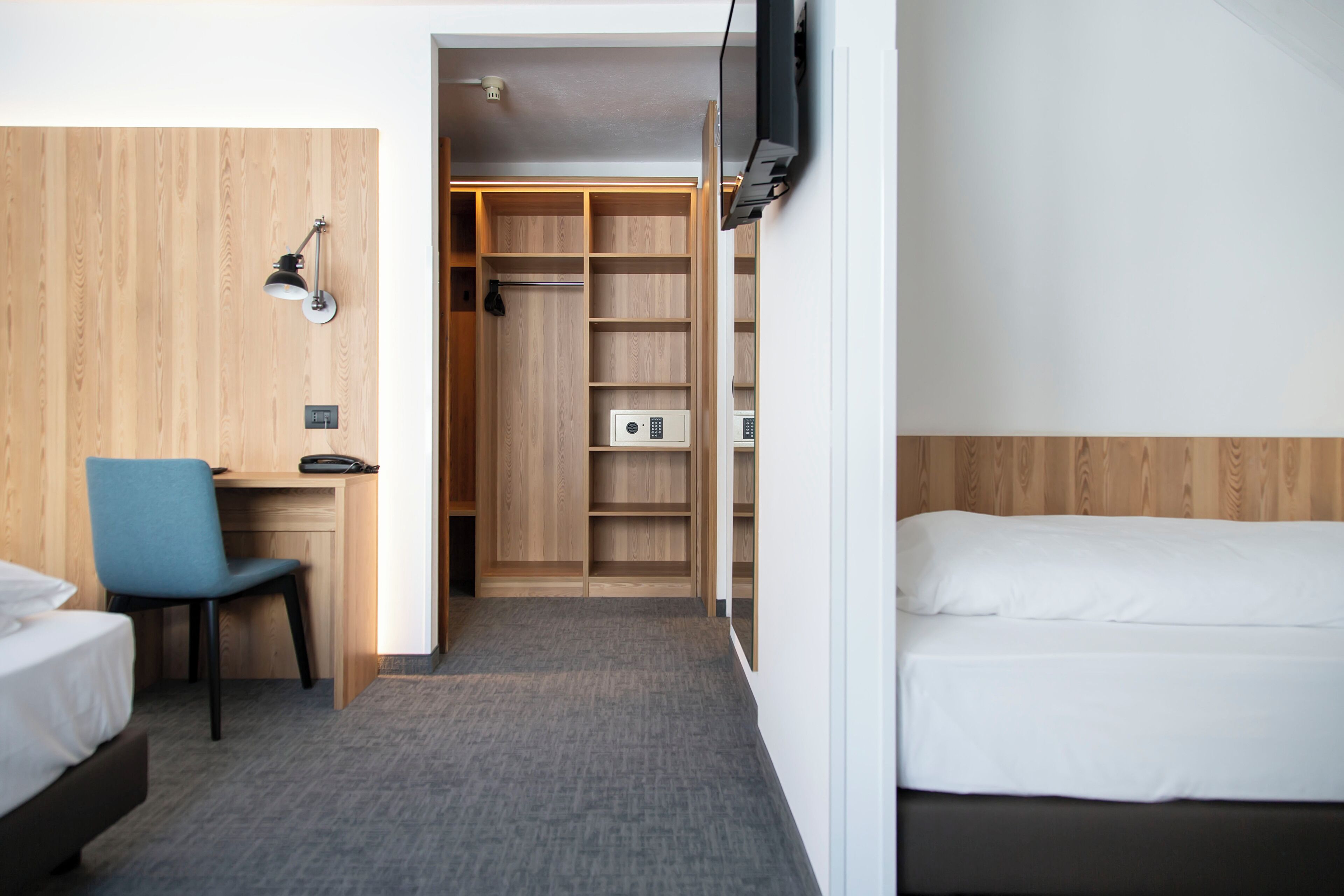 Habitació d'hotel amb un llit, un escriptori amb una cadira, un armari i una televisió penjada a la paret.