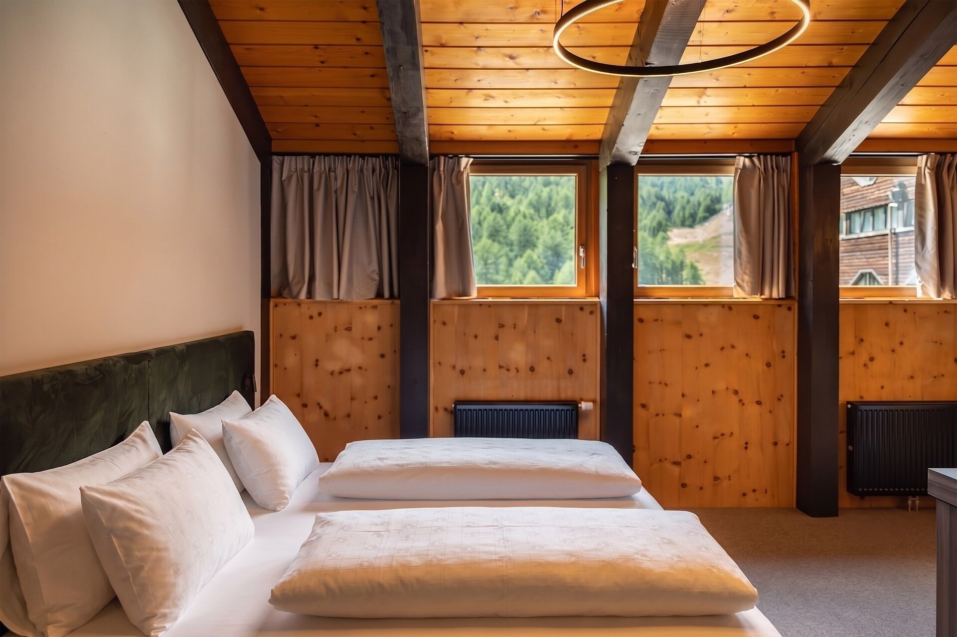 Een slaapkamer met een houten plafond, twee bedden met witte lakens, een radiator en een raam met gordijnen.