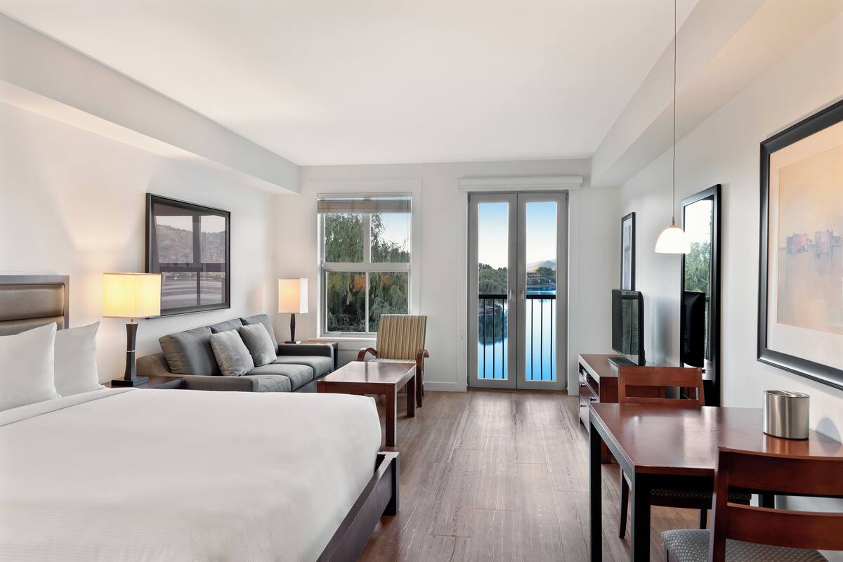Une chambre d’hôtel avec un grand lit, un canapé, une table à manger et un téléviseur. Elle dispose de fenêtres et d’un balcon avec vue.